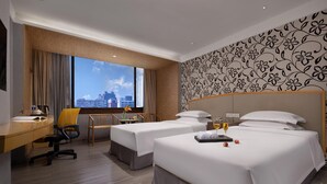 Une chambre d’hôtel avec deux lits, un bureau, une chaise et une grande fenêtre donnant sur la ville.