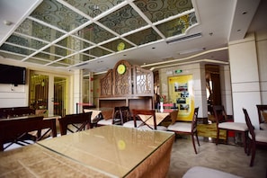 Un restaurant avec un plafond haut, des panneaux de verre décoratifs, des meubles en bois et une horloge au mur.