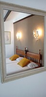 Un dormitorio con cabecera de madera, dos camas con almohadas blancas y mostaza, y lámparas fijadas a la pared.