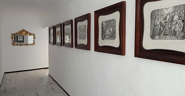 A hallway with framed artwork on the wall and a mirror with an ornate frame. - Hostal Ca's Bombu (Capdepera)
