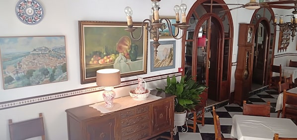 Un comedor con suelo de cuadros, muebles de madera y una pared decorativa con obras de arte enmarcadas.