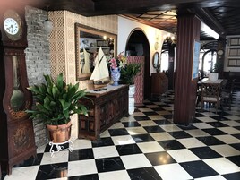 Un vestíbulo con piso a cuadros, muebles de madera, un espejo grande y relojes.
