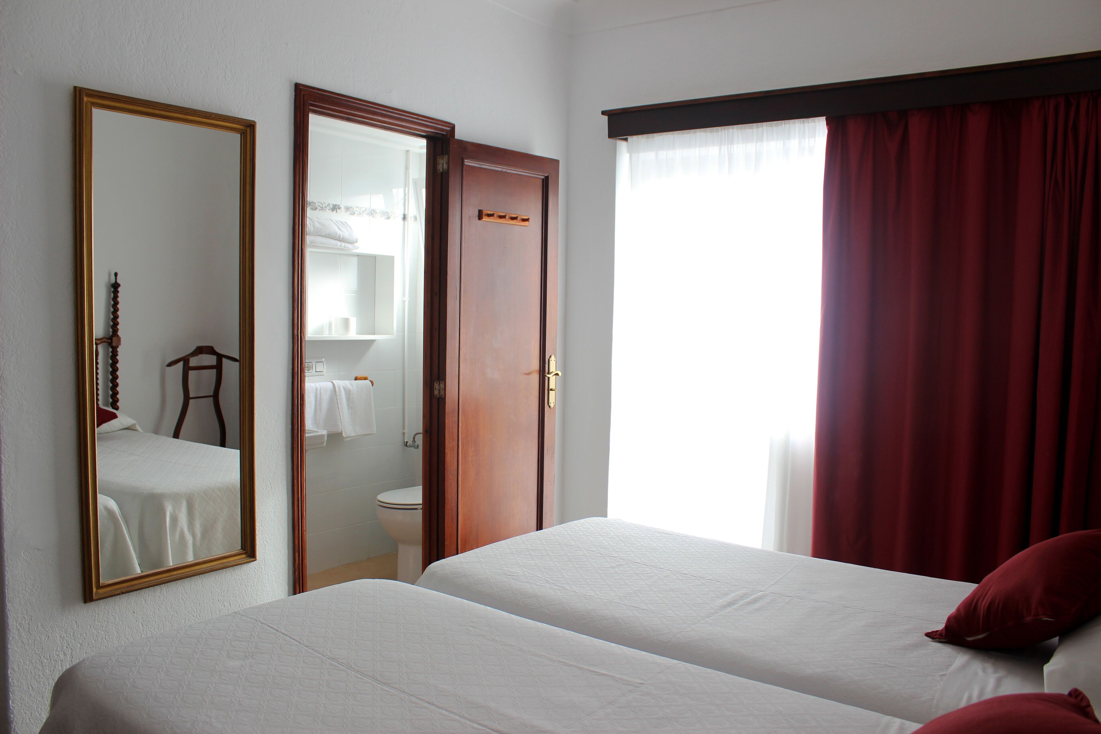 A hotel room with two beds, a bathroom with a toilet and sink, and a large mirror.