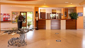 A reception area with a glass table, wooden reception desk, and a potted plant. - Kathrin Beach Hotel (ADELIANOS KAMPOS)
