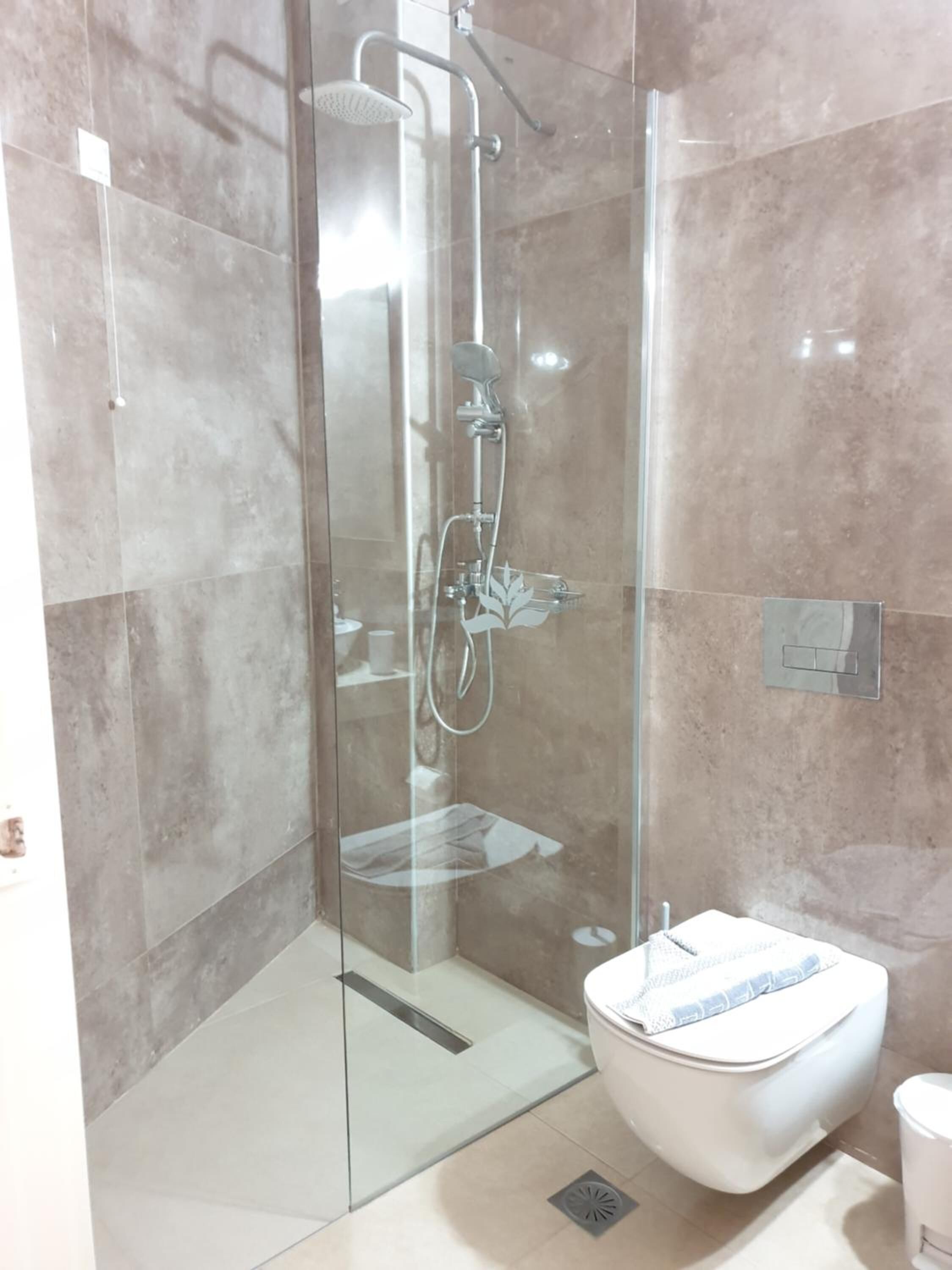 A modern bathroom with a glass-enclosed shower, a white toilet, and a tiled floor.