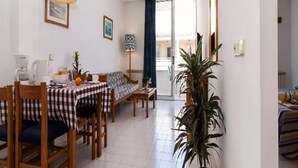 A dining area with a checkered tablecloth, wooden chairs, a sofa, and a potted plant. - Apartamentos ES Trenc (Ses Salines)