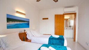 A hotel room with two beds, a painting of a beach, a wooden door, and a kitchenette. - Apartamentos ES Trenc (Ses Salines)