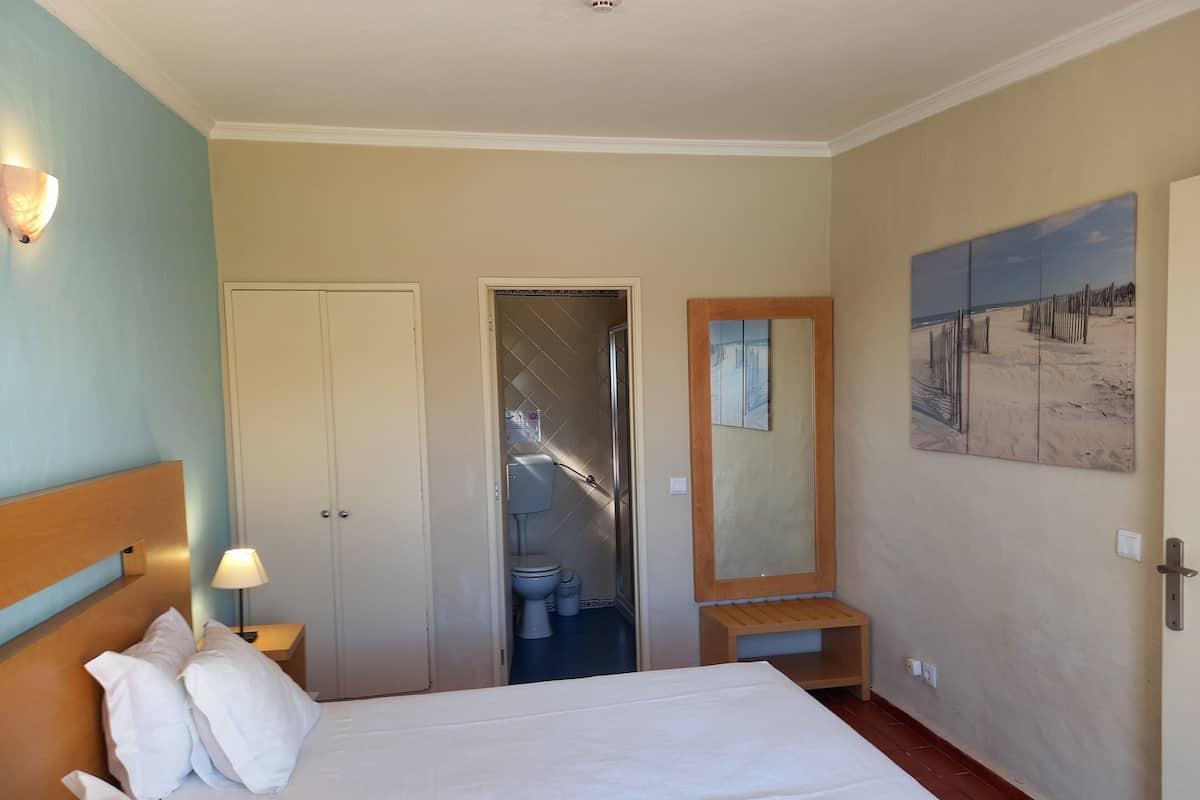 Ein Hotelzimmer mit einem Bett, einem Nachttisch, einem Wandspiegel und einem Bild mit einer Strandansicht.