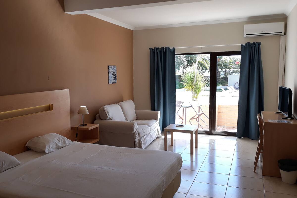 Ein Hotelzimmer mit Bett, Sofa, Schreibtisch mit Fernseher und Balkon mit Blick ins Freie.