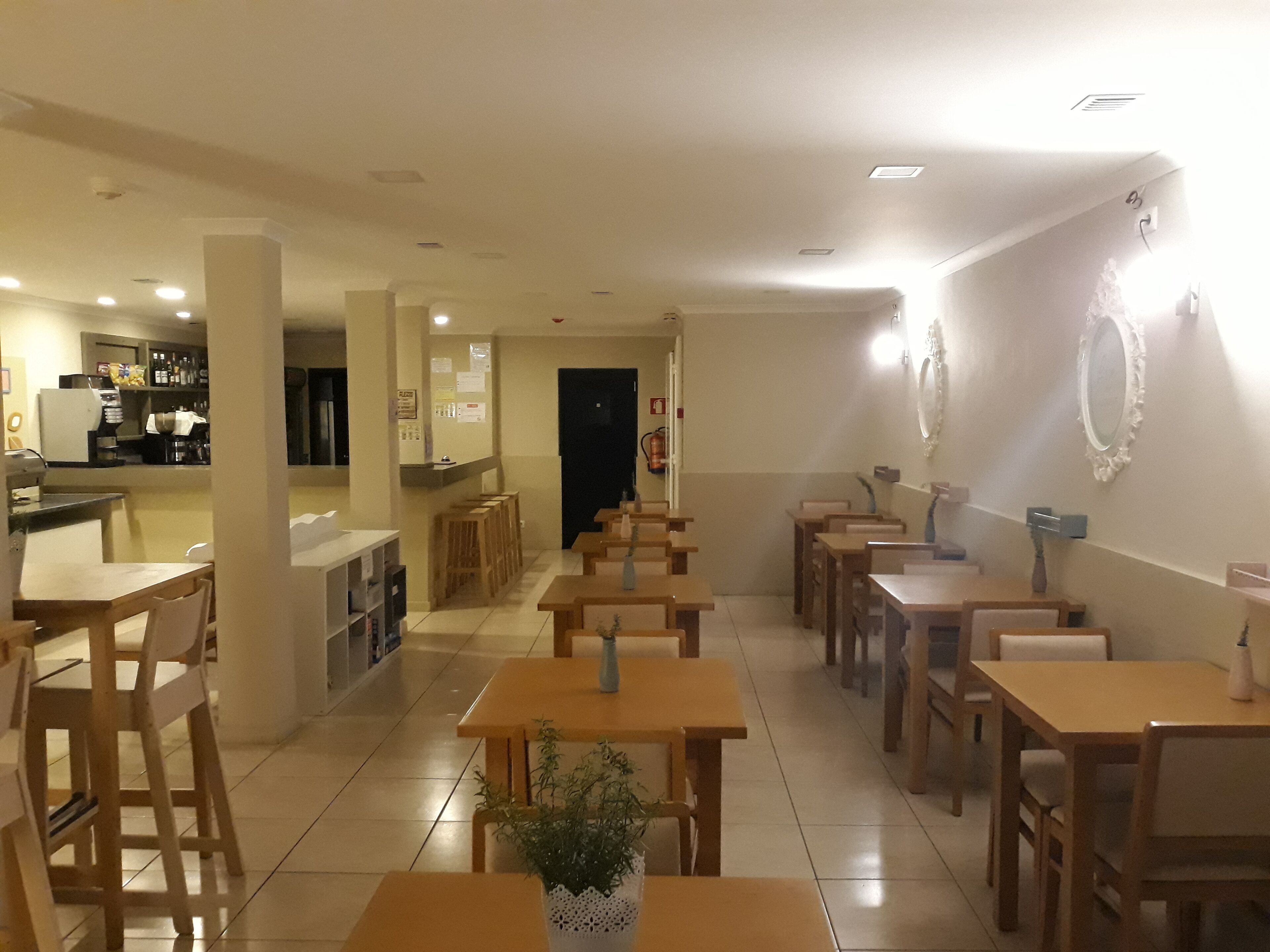 Un restaurante con mesas y sillas de madera, una barra con caja registradora y una zona de cocina al fondo.