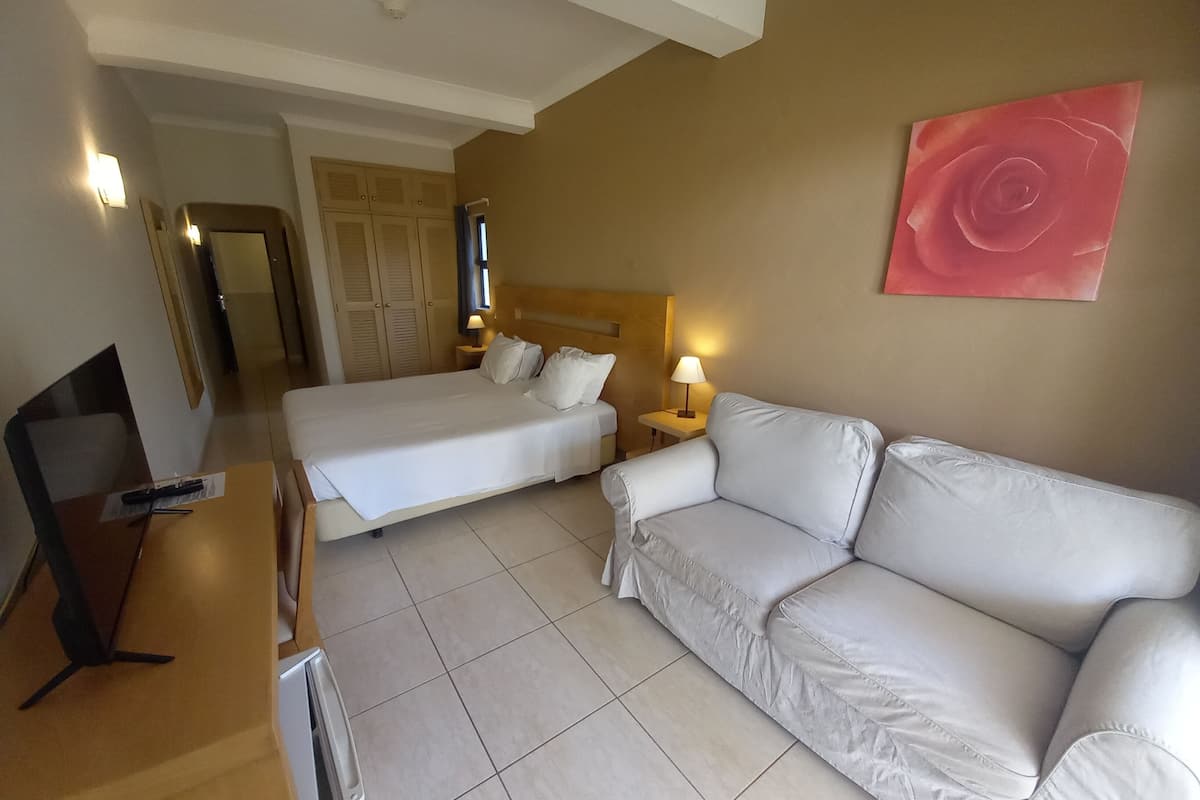 Ein Hotelzimmer mit zwei Betten, einem Sofa, einem Schreibtisch mit Computer und einem Fernseher.