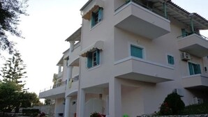 A multi-story residential building with balconies, a stone wall, and a garden area. - Apartments Villa Frangis (Corfu)