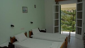 A room with two single beds, a small table, and a window with a view of greenery and buildings. - Apartments Villa Frangis (Corfu)