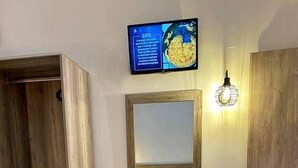 Habitación de hotel con un armario de madera, una mesita de noche con una botella y vasos, un espejo y dos toallas sobre la cama.