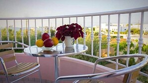 Un balcón con una mesa dispuesta para dos personas, con una cesta de frutas y una planta en maceta.