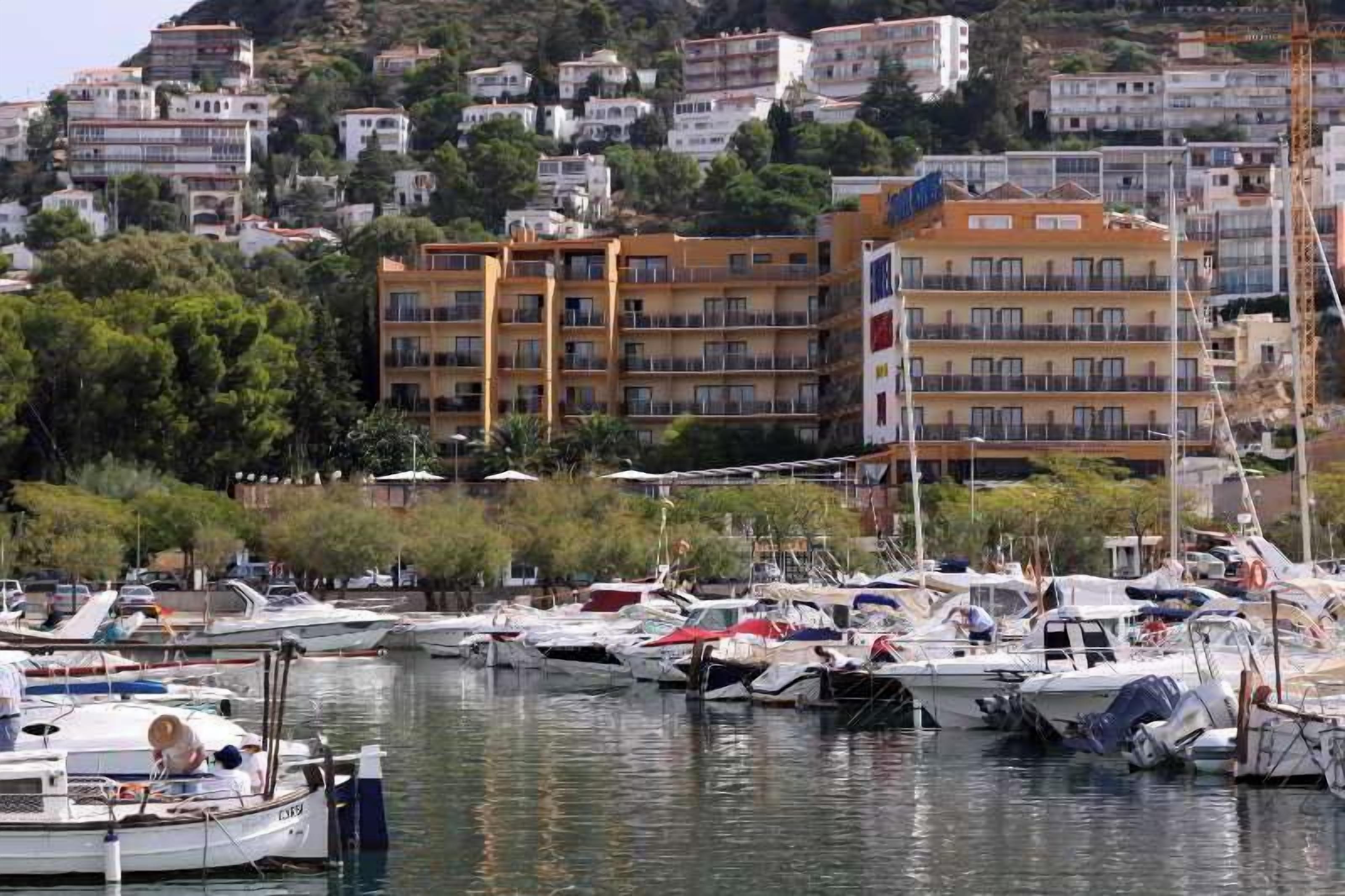 Un port de plaisance avec des bateaux amarrés, entouré de bâtiments dotés de balcons et bordé par des collines.