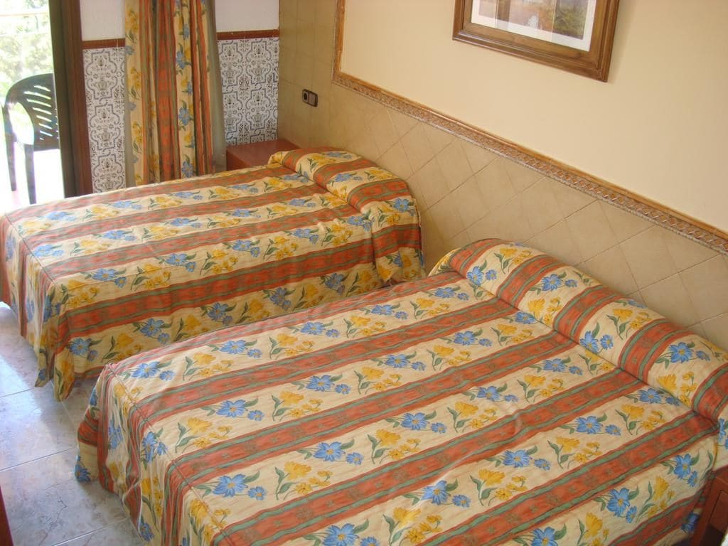 A room with two beds with floral bedding, a chair, and a patterned wall.