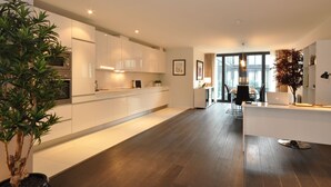 Una cocina moderna con armarios blancos, una zona de comedor con mesa y sillas, y una planta grande en maceta.