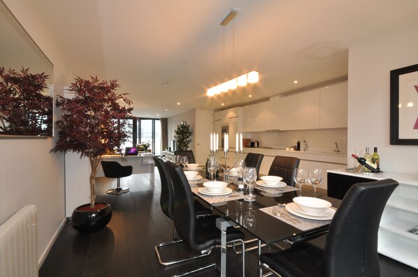 A modern dining area with a long table set for six, black chairs, and a potted plant. - Your Base Apartments Dublin (Dublin)