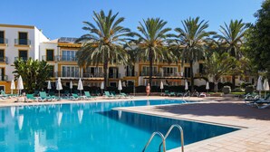 A swimming pool with lounge chairs and umbrellas, surrounded by palm trees and a hotel building. - Quinta do Morgado - Monte da Eira (Tavira)