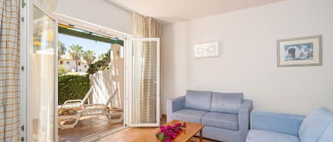 A living room with a blue sofa, a wooden coffee table with flowers, and a sliding glass door leading to an outdoor area with chairs.