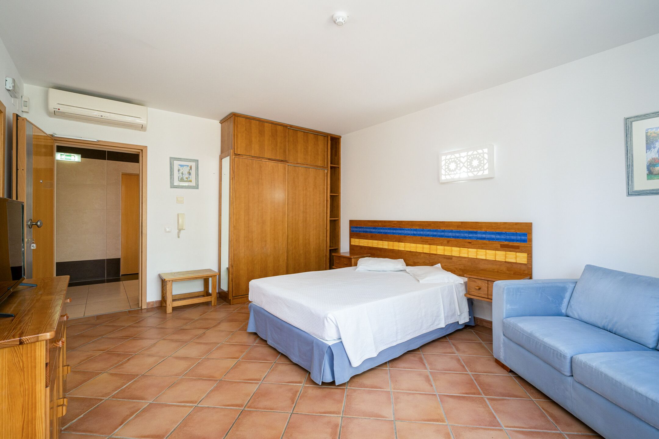 Une chambre d’hôtel comprenant un lit, un canapé, une armoire en bois, un banc et un bureau.