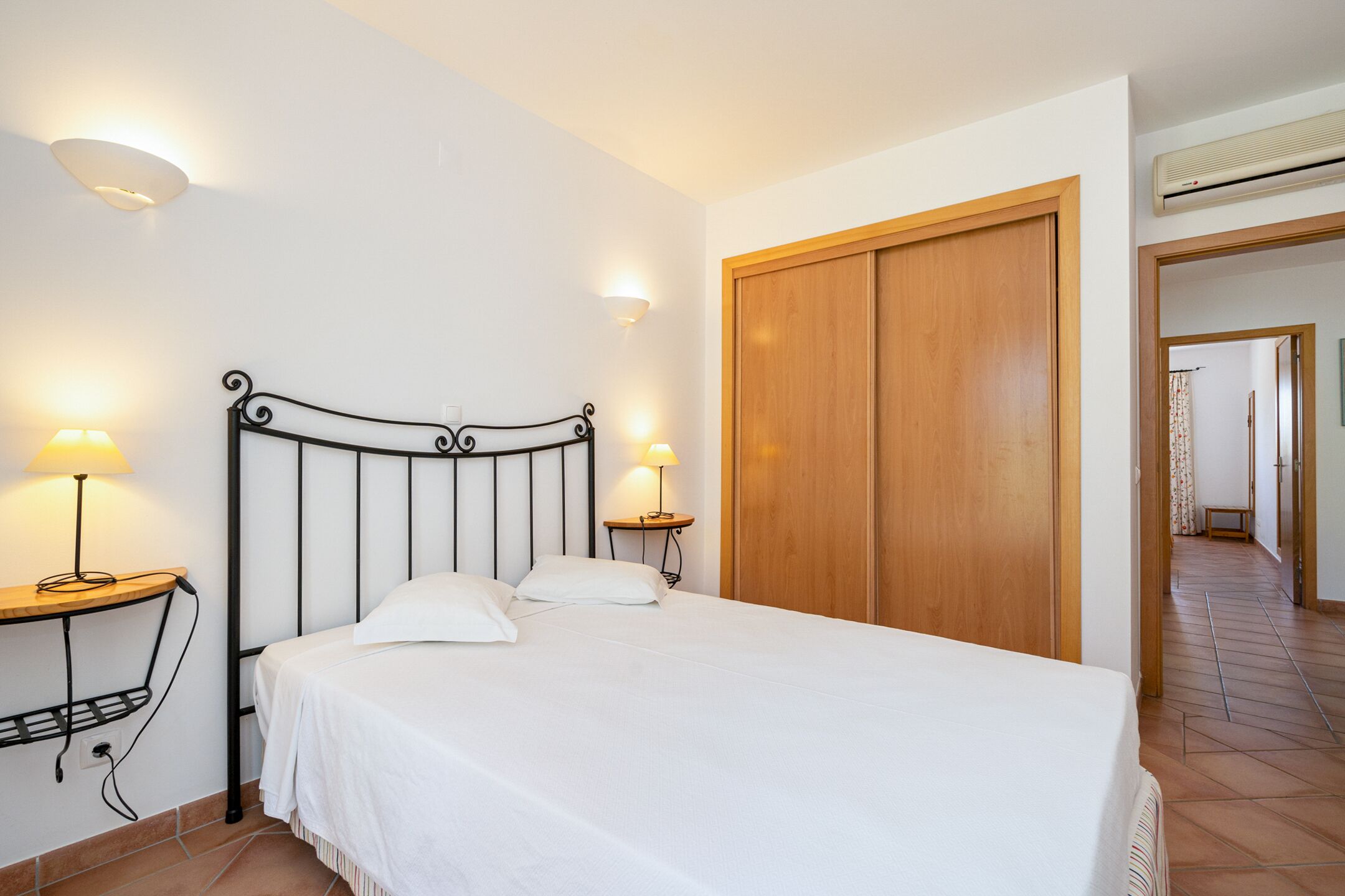 Ein ordentlich bezogenes Bett mit weißen Bettwäsche, zwei Nachttischlampen und einem Holzschrank.