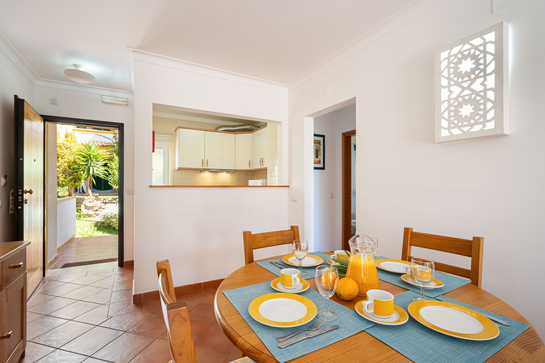A dining area with a round table set for breakfast, including plates, cutlery, and a pitcher of orange juice.