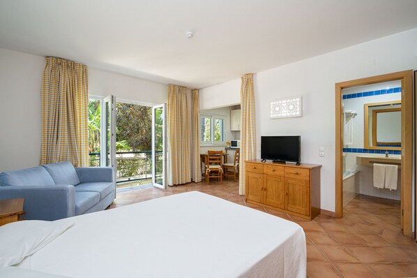 A hotel room with a bed, a TV, a wooden cabinet, a sofa, a dining table, and a bathroom with a mirror and sink.