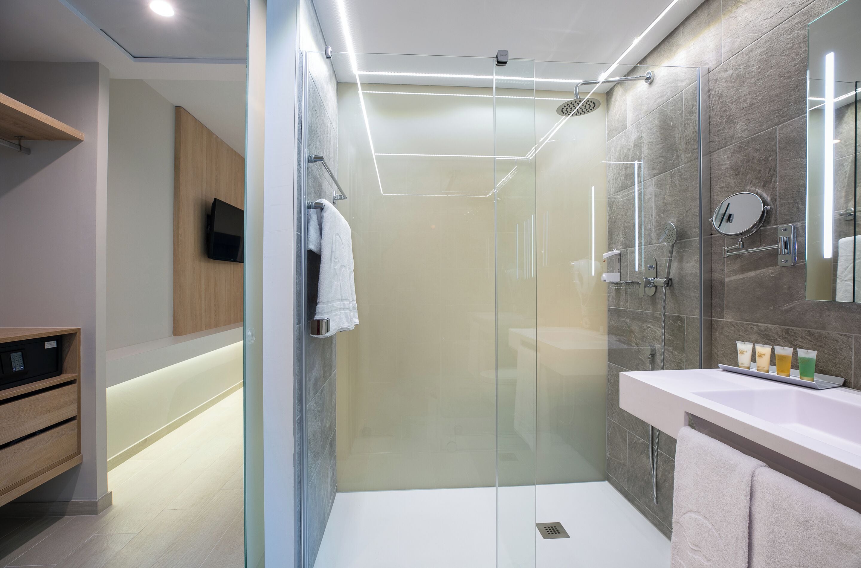 A modern bathroom with a glass-enclosed shower, a vanity with a mirror, and a shelf with toiletries.