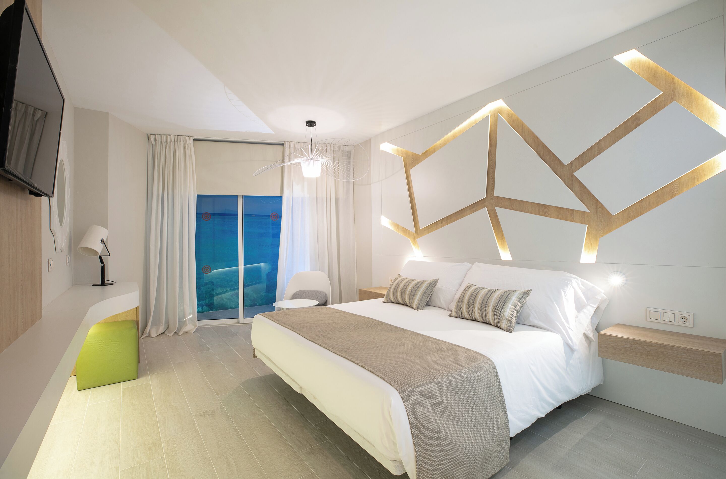 Habitación de hotel moderna con una cama grande, un escritorio, una silla, un televisor y vista al mar.