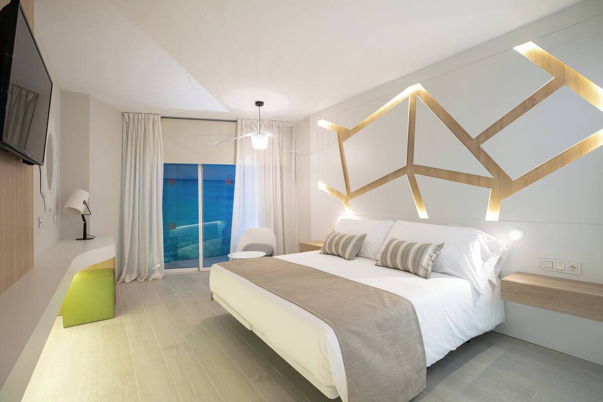 Habitación de hotel moderna con una cama grande, un escritorio, una silla, un televisor y vista al mar.