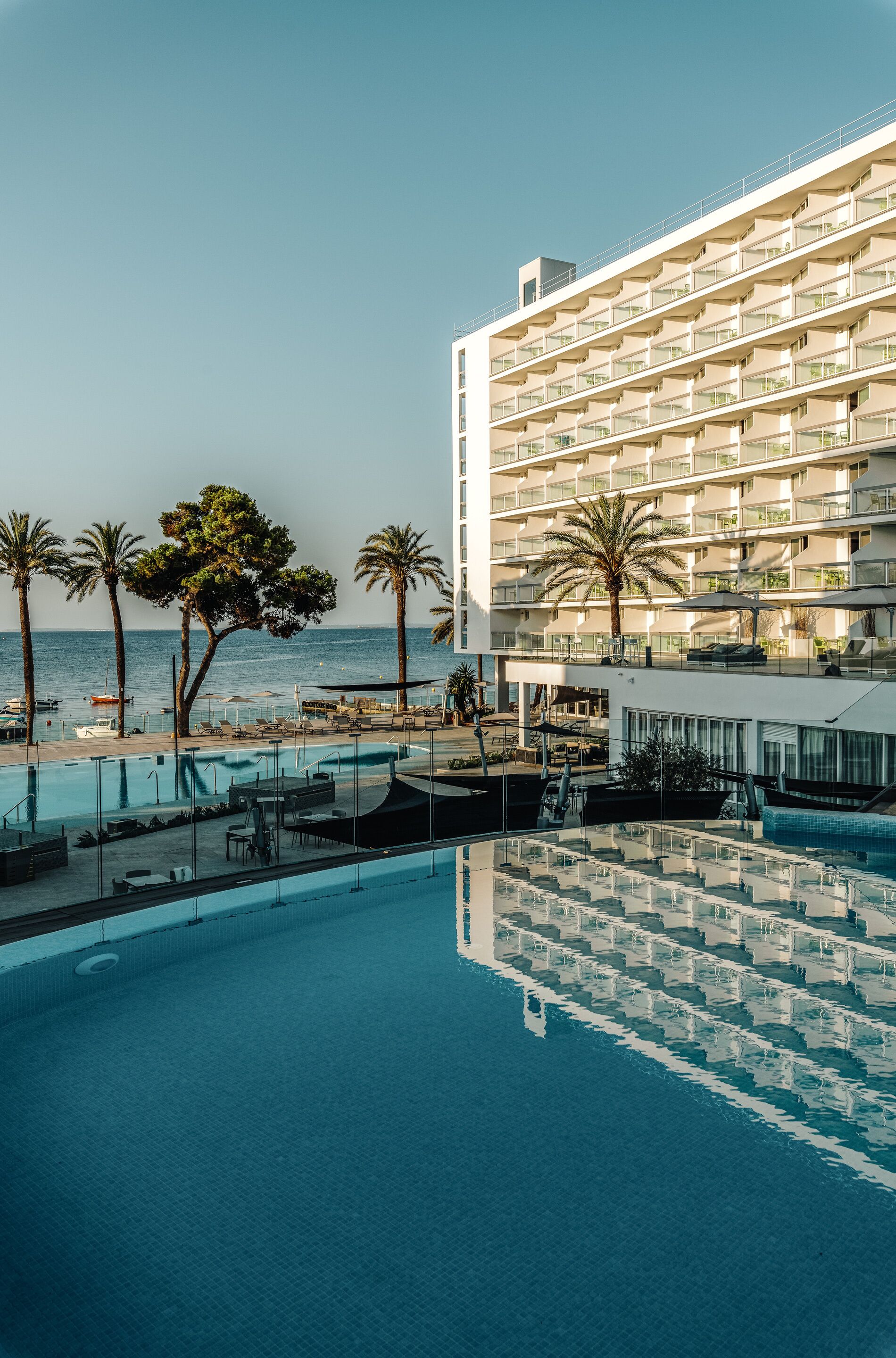 A hotel with a pool, palm trees, and a view of the sea.