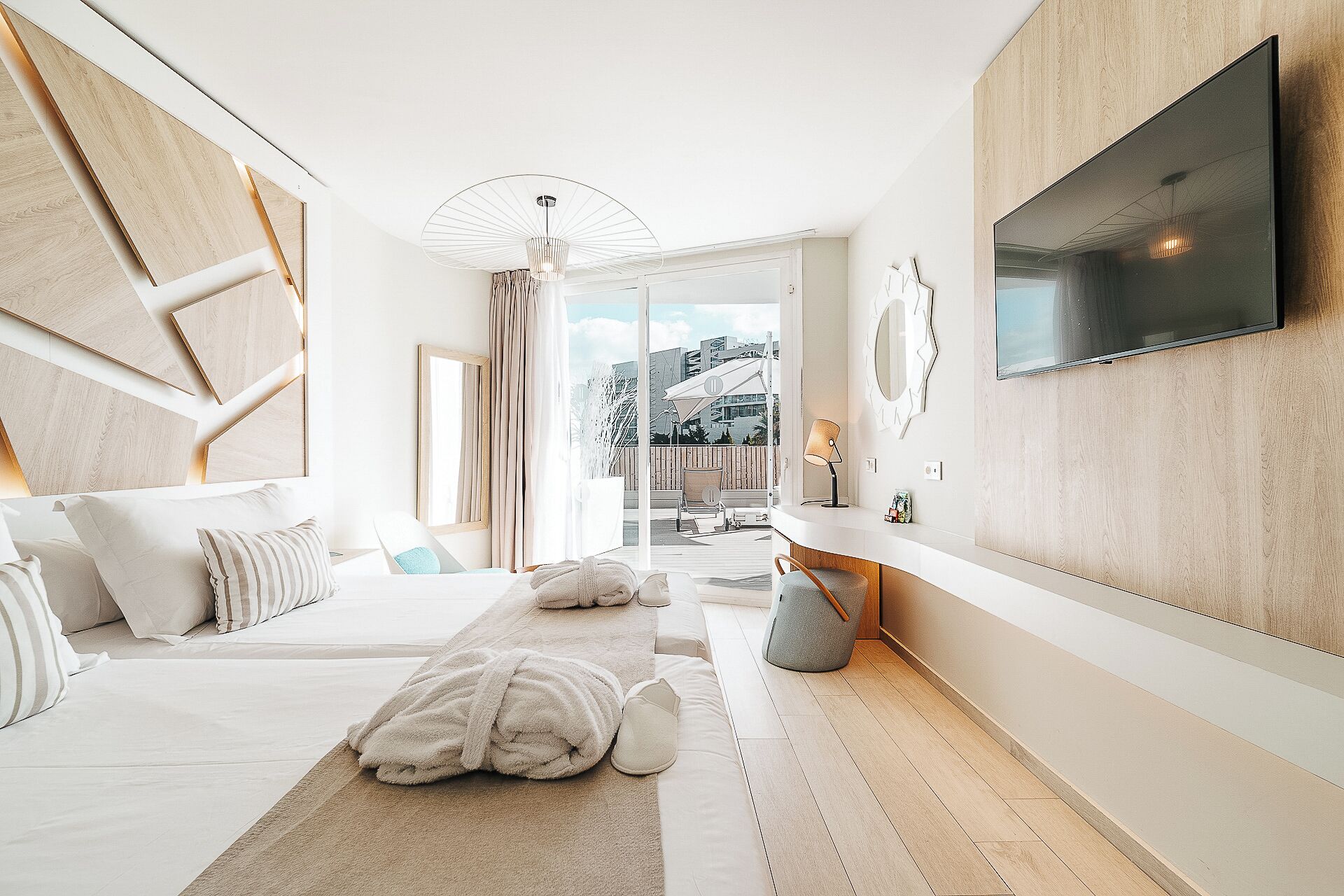 Habitación de hotel moderna con una cama grande, un televisor montado en la pared y vistas al exterior.