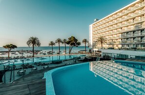 Un hotel con piscina que domina la playa, palmeras y el mar.