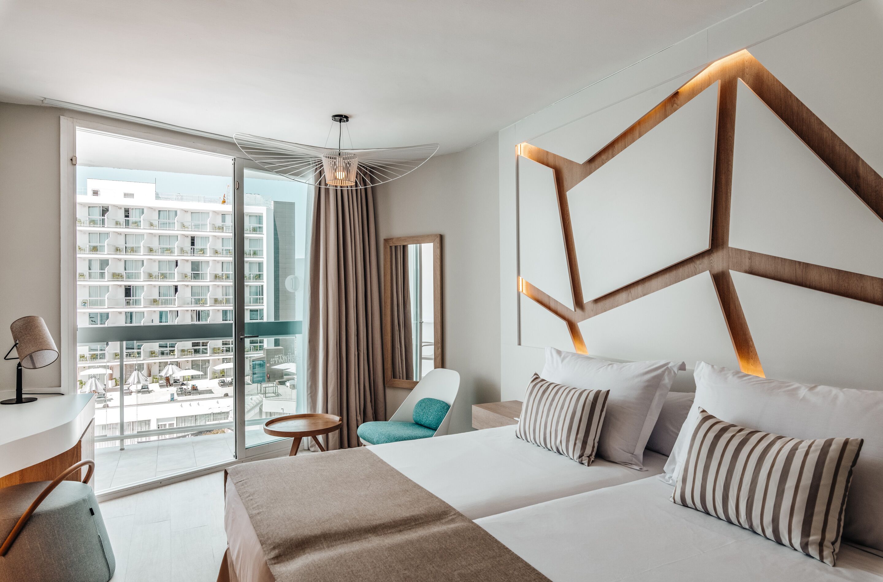 A modern hotel room with a large bed, a desk, and a view of a building through the window.