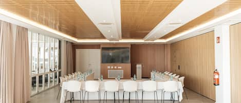 Ein Konferenzraum mit langem Tisch, weißen Stühlen, einer großen Leinwand und einer Holzwanddecke.