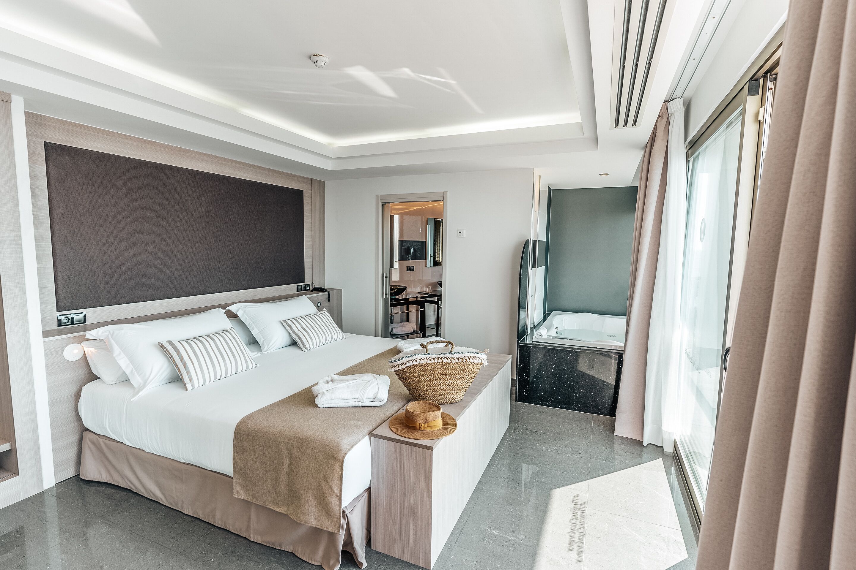 Een moderne hotelkamer met een groot bed, een nachtkastje met een mand, en uitzicht op de badkamer.