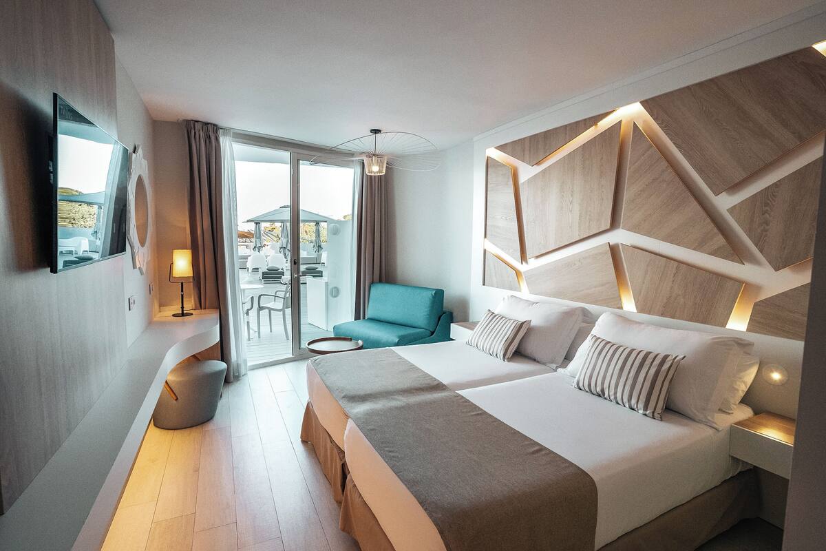 Une chambre d’hôtel moderne dotée d’un grand lit, d’un coin salon avec un fauteuil de couleur turquoise et offrant une vue sur l’extérieur.