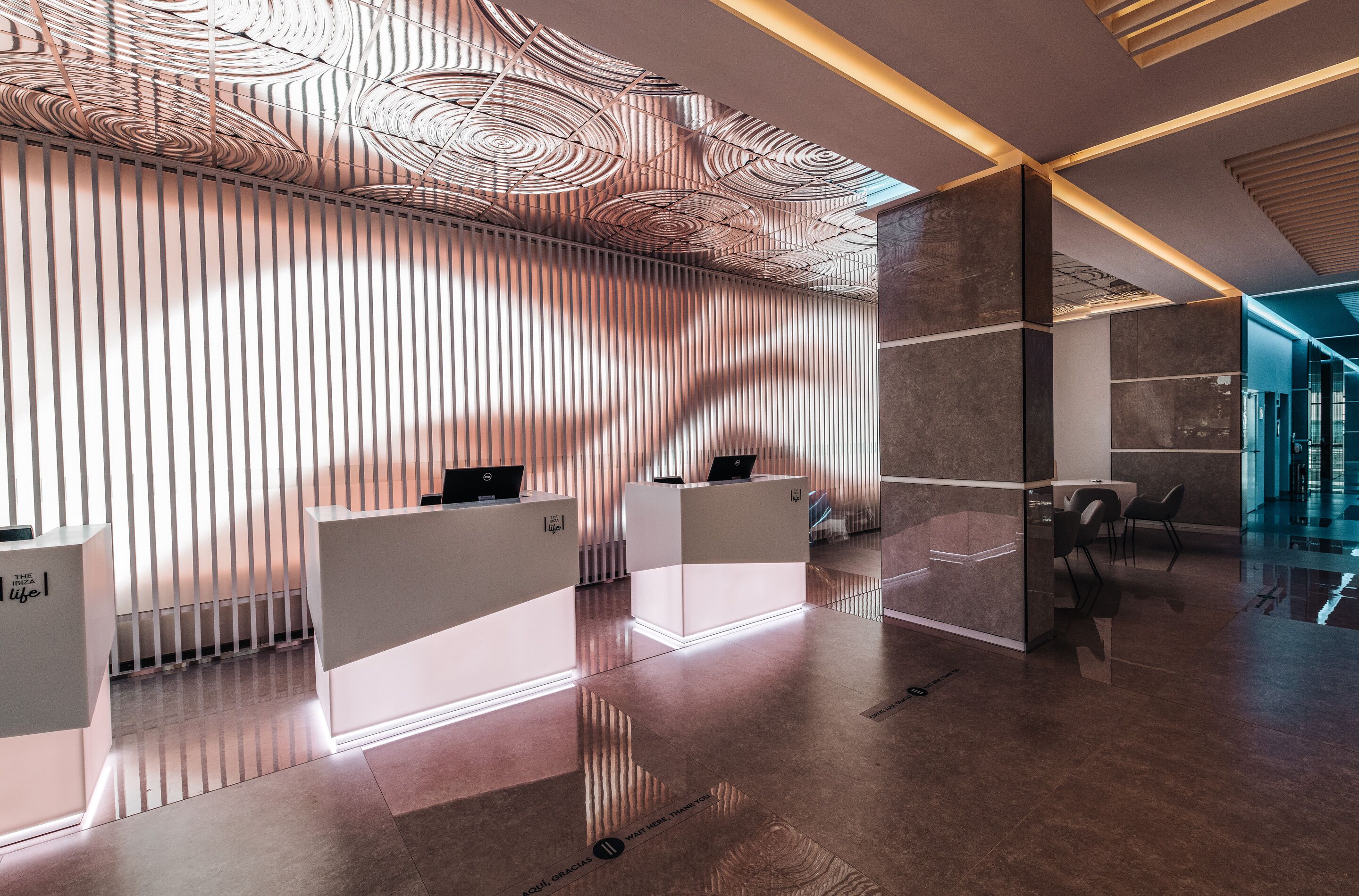 A modern reception area with a unique ceiling design, a reception desk, and a waiting area with chairs.