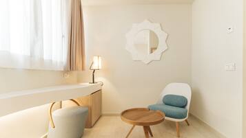 Una habitación moderna con una mesa redonda de madera, una silla blanca con cojín azul, un taburete pequeño y redondo, un espejo montado en la pared y una lámpara de noche.