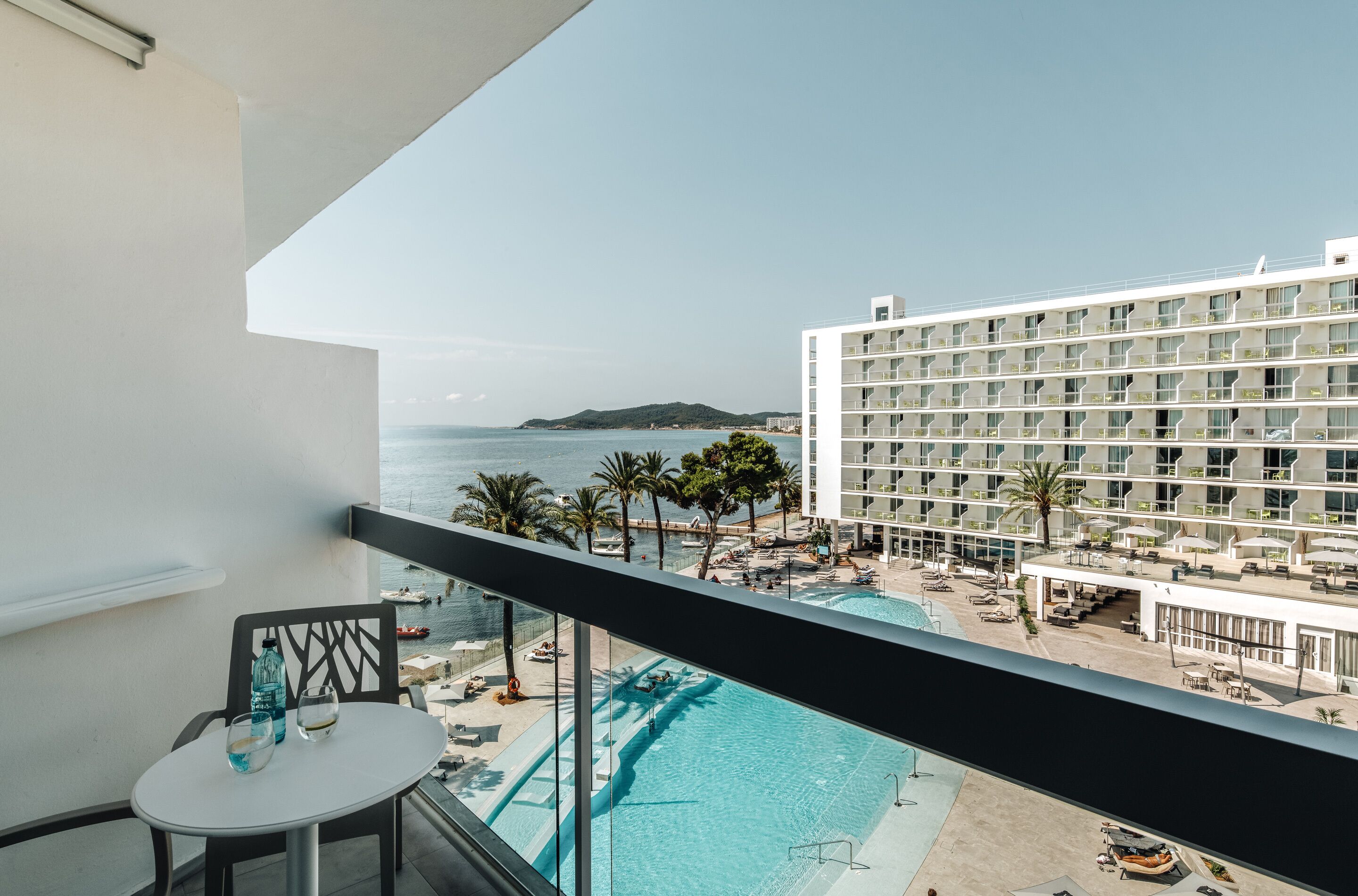 A balcony with a view of a swimming pool, a hotel building, and a distant island.
