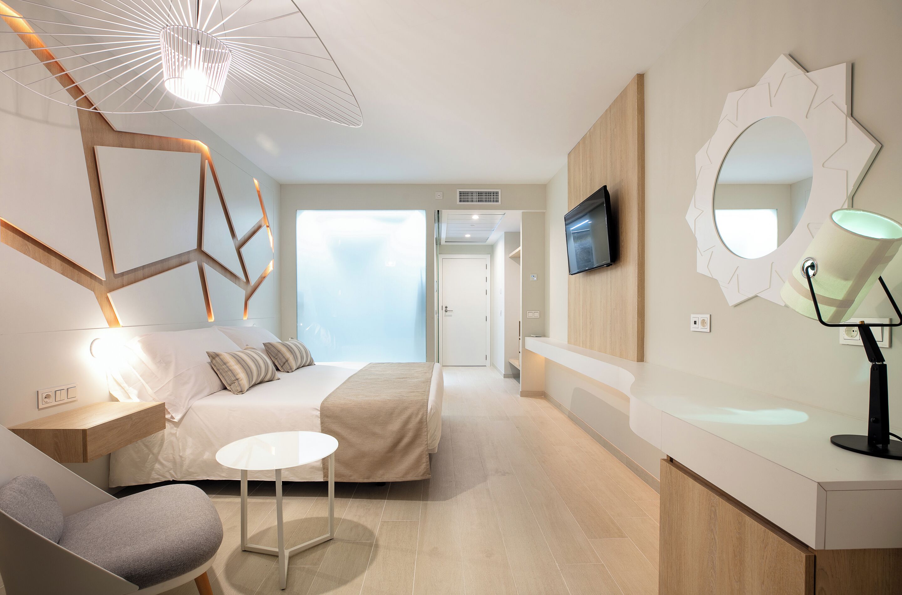 Una habitación de hotel moderna con cama, mesita de noche, silla, mesa redonda y televisor montado en la pared.