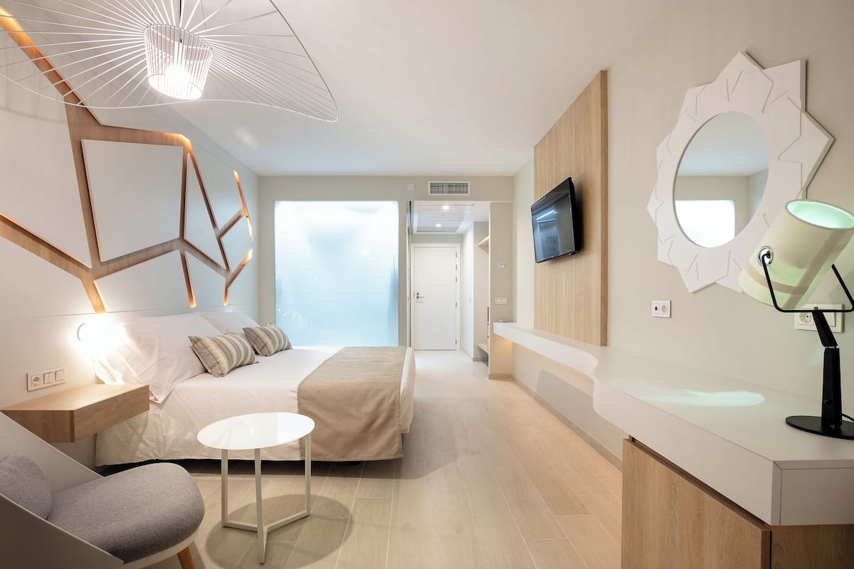 Una habitación de hotel moderna con cama, mesita de noche, silla, mesa redonda y televisor montado en la pared.