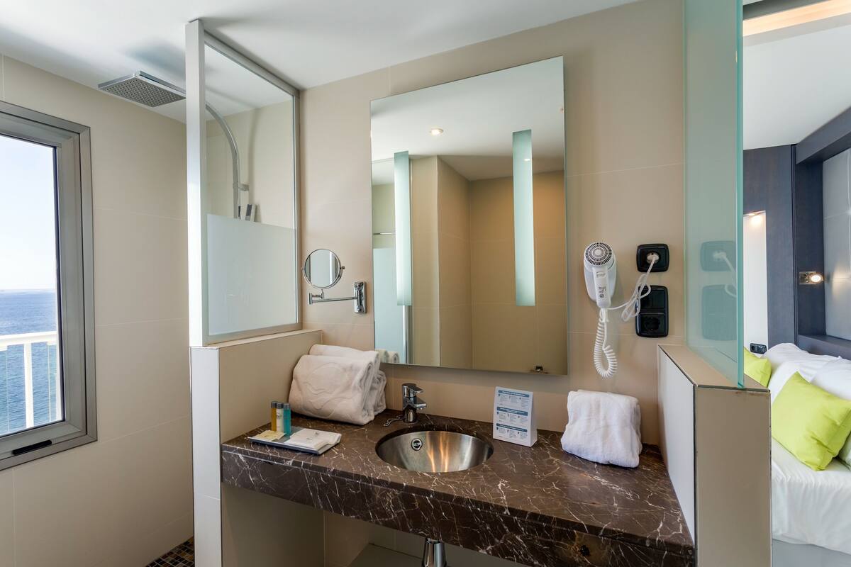 Une salle de bain moderne avec un lavabo en marbre, un grand miroir, un sèche-cheveux et un porte-serviettes.