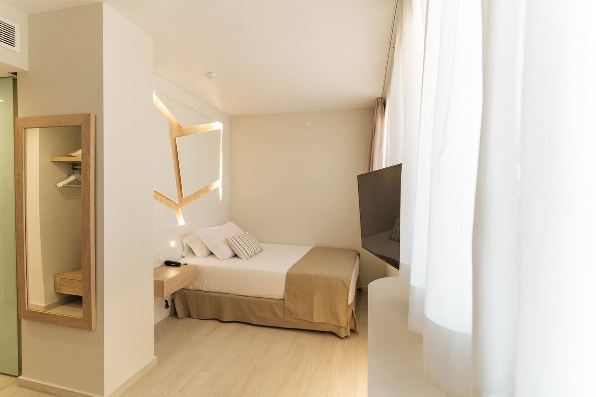 Une chambre d’hôtel avec un lit, une table de chevet, une télévision et un miroir.