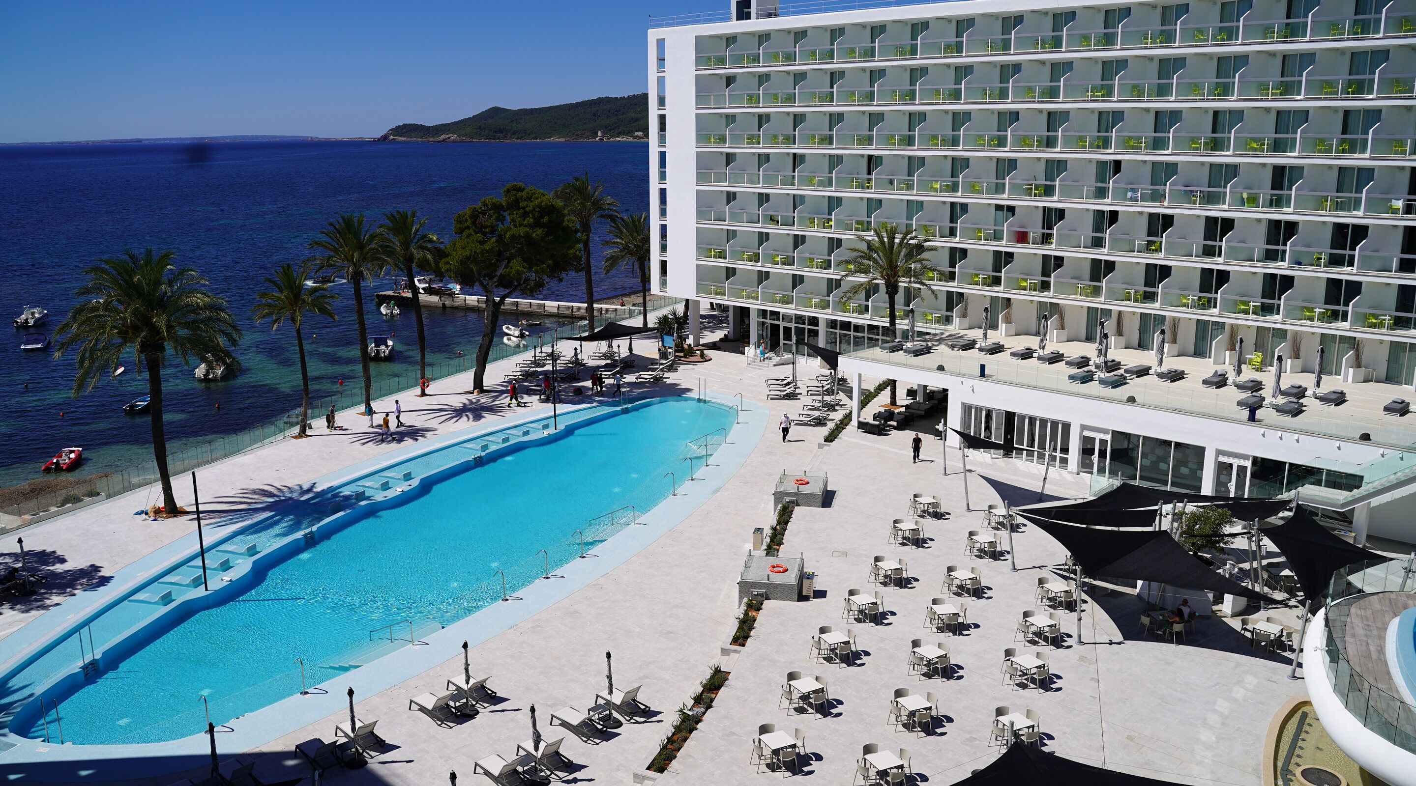 A hotel with a pool, sun loungers, and a view of the sea.