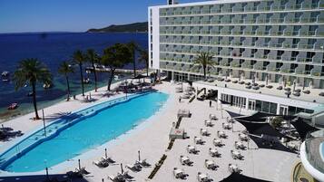 A hotel with a pool, sun loungers, and a view of the sea.