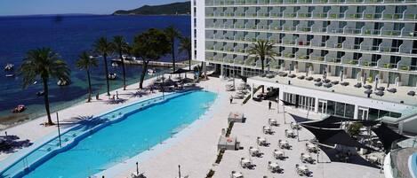 A hotel with a pool, sun loungers, and a view of the sea.