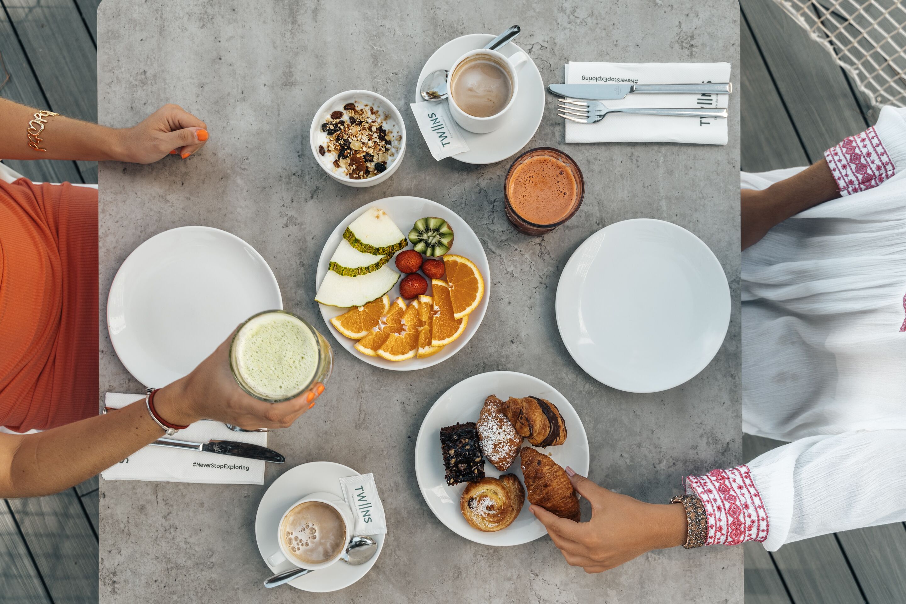 Een tafel met diverse etenswaren en drankjes, waaronder een bord fruit, een schaaltje granola en een kop koffie.